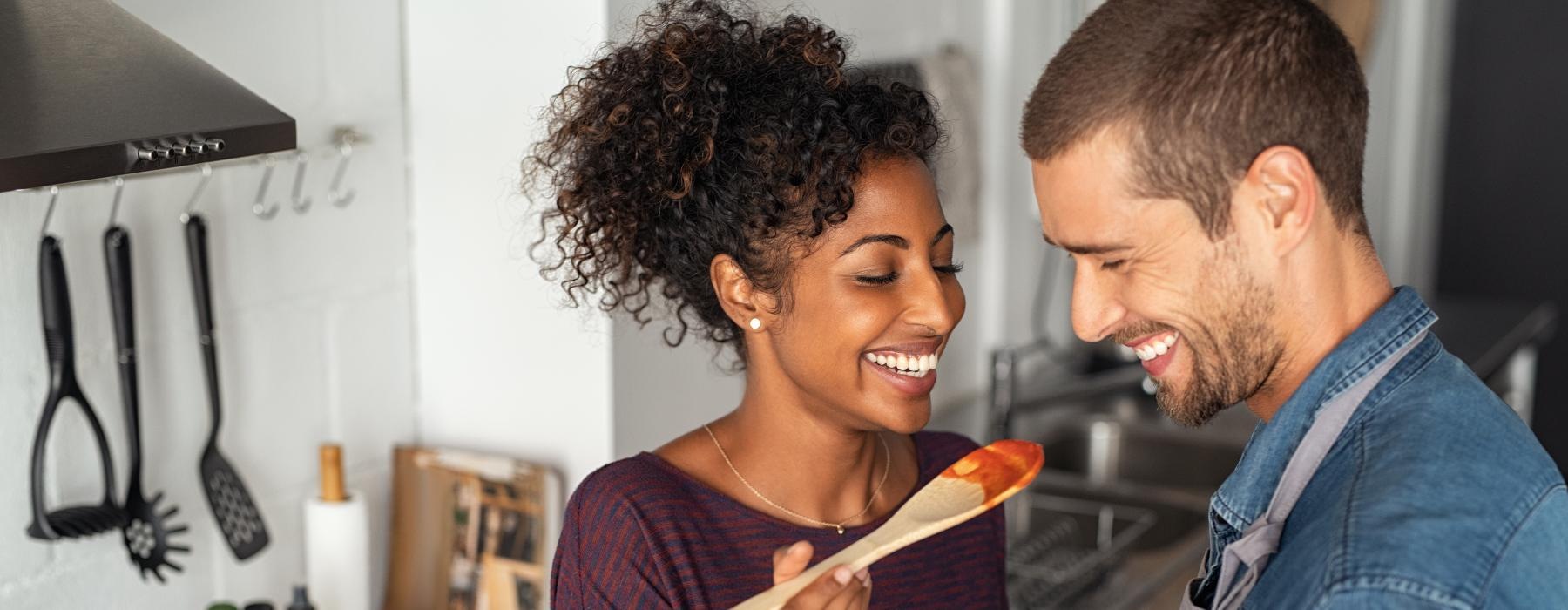 a man and a woman smiling and tasting pasta sauce
